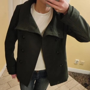 Mörkgrön kappa - Säljer en snygg mörkgrön kappa i mycket bra skick. Den har en klassisk design med stora knappar och en bred krage. Perfekt för höst och vår, och ger en stilren look. Passar bra till både vardag och lite finare tillfällen.❤️💋