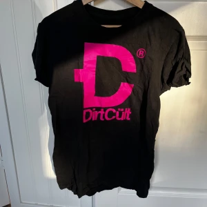 Svart t-shirt från DirtCult - Säljer en svart t-shirt från DirtCult i storlek S. Den har en stor rosa logga på framsidan som verkligen poppar!T-shirten är i bra skick och gjord av mjukt material. Kan fås med gratis med ett annat plagg!  Varan finns i Enköping och jag har möjlighet att mötas upp alternativt posta emot frakt!💞 Vid intresse kan flera detaljerade bilder skickas/ bilder med tröjan på! Tvättas innan den säljs!😍