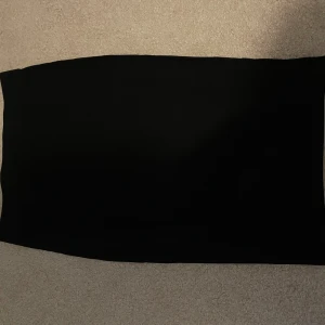 Svart kjol - Säljer en stilren svart kjol i bra skick. Perfekt för både vardag och festliga tillfällen. Kjolen har en klassisk design som gör den lätt att matcha med olika toppar och accessoarer. Ger kroppen en fin form. (Har dock fått några få prickar av klorin) 