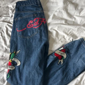 Blå jeans med Ed Hardy-design - Snygga blå jeans från Ed Hardy i storlek XS. De har coola tatueringsinspirerade broderier och ett stort rött Ed Hardy-tryck på baksidan. Byxorna är sparsamt använda!💜 Kontakta mig vid frågor men använda gärna ”Köp” om ni vill köpa. 