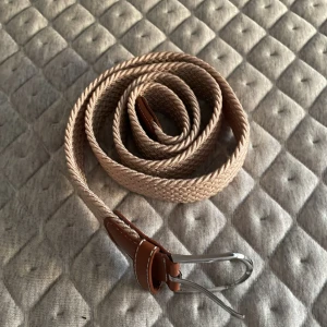 Beige flätat bälte med bruna detaljer - Säljer ett snyggt beige flätat bälte med bruna läderdetaljer och en silverfärgad spänne. Perfekt för att ge en stilren touch till din outfit. Passar både till vardags och fest. Justerbar längd för bästa passform.