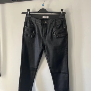 Helt nya Svarta byxor med dragkedjor från Luizacco - Helt nya snygga svarta byxor i skinnimitation från Luizacco. De har flera coola dragkedjor framtill som ger en edgy look. Perfekta för en utekväll eller när du vill känna dig extra stylish. Byxorna har en tight passform och är helt nya. 