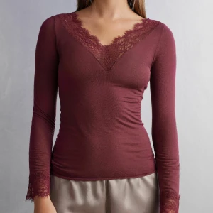 Vinröd långärmad topp med spetsdetaljer - Säljer en elegant vinröd topp med långa ärmar och v-ringad spetsdetalj. Perfekt för höst och vinter, den är både stilren och bekväm. Passar bra till både vardag och festliga tillfällen. Toppen har en tight passform som framhäver figuren. Nypris 550. Ser helt ny ut och använt ganska få gånger. 