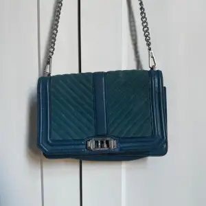 Snygg blå axelväska från Rebecca Minkoff i mycket bra skick. Väskan har ett quiltat mönster och en stilren kedjerem. Den är gjord av skinn och mocka, vilket ger en lyxig känsla. Perfekt för både vardag och fest!