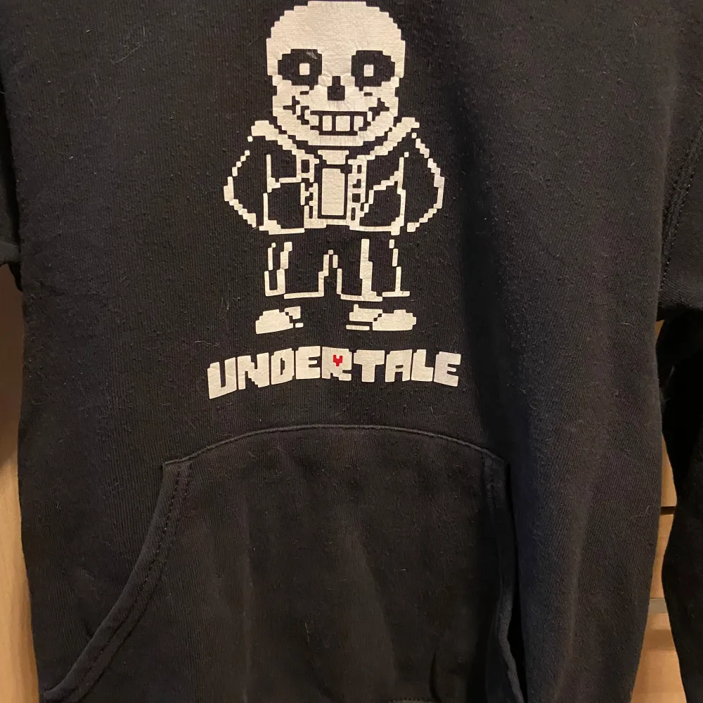 Säljer en svart hoodie med Undertale-tryck på framsidan. Den har en stor ficka fram och en mysig huva. Perfekt för fans av spelet! Tröjan är i bra skick och passar perfekt för höst och vinter.. Hoodies.