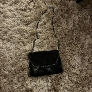 Svart axelväska med kedjedetaljer - Snygg svart axelväska, med snyggt print på insidan. Perfekt för alla tillfällen 💗