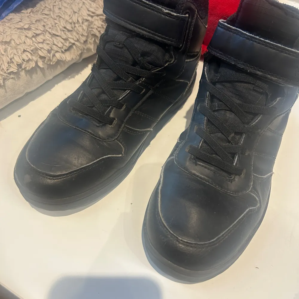 Säljer ett par svarta sneakers i skinn med snörning och kardborreband. De är vattentäta och har en robust sula, perfekt för höst och vinter. Skorna är i bra skick och redo för nya äventyr!. Skor.