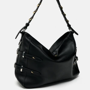 Svart axelväska med gulddetaljer - Snygg svart axelväska i skinn med gulddetaljer och justerbar axelrem. Väskan har flera spännen på sidorna och en dragkedja upptill för säker förvaring. Perfekt för både vardag och fest! Nyskick! 