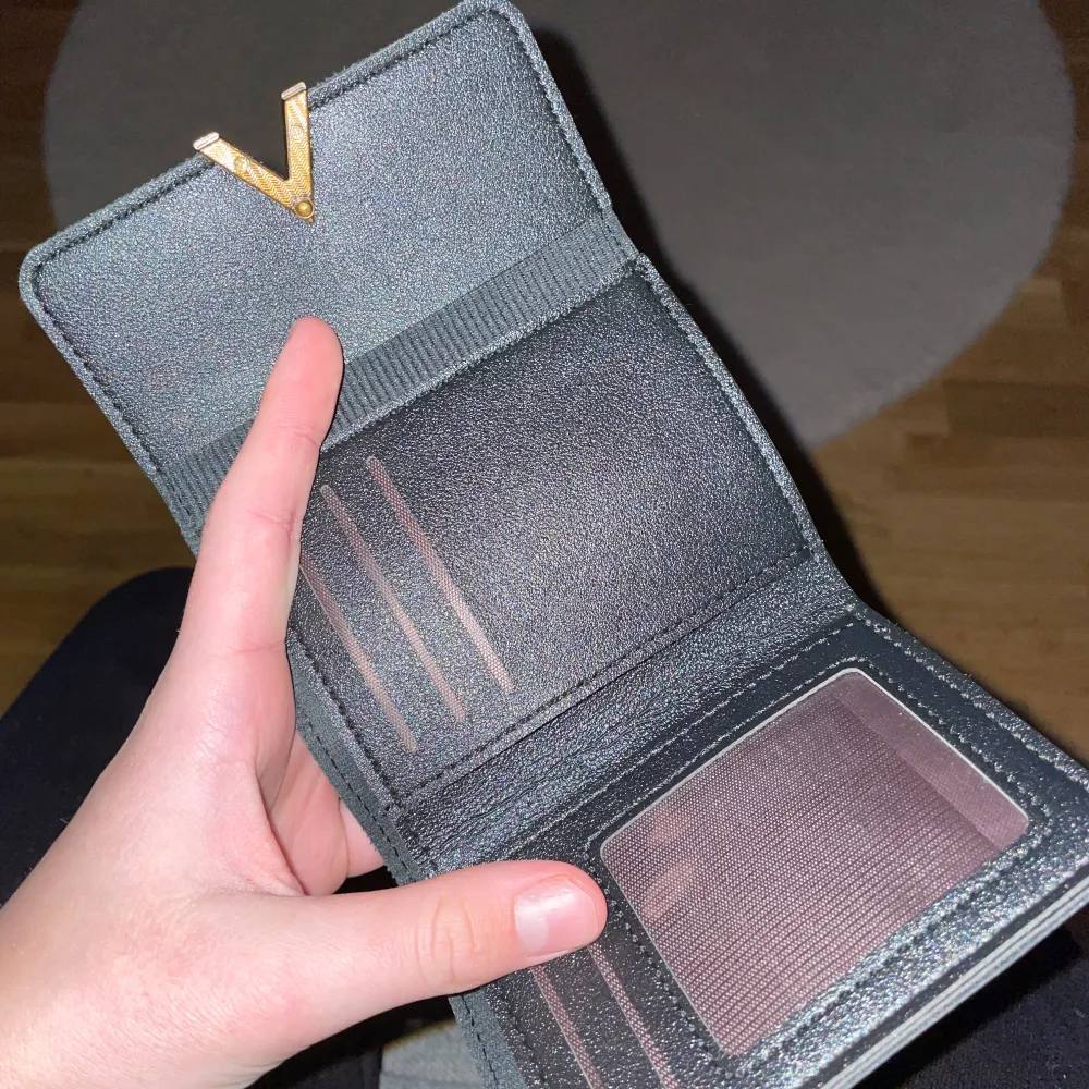 Säljer en stilren svart plånbok med en snygg guldfärgad detalj på framsidan. Plånboken har flera fack för kort och ett genomskinligt fack för ID eller bilder. Perfekt för att hålla ordning på dina kort och kontanter. Passar både till vardags och fest!. Asusteet.
