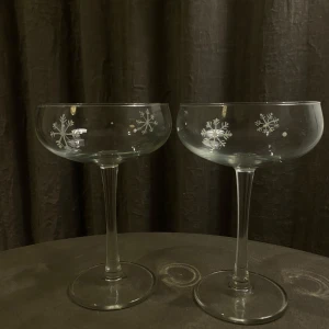 Cocktailglas med snöflingor  - Två eleganta champagneglas med ett vackert snöflingemönster. Perfekta för vinterfester eller som en fin detalj på julbordet. Glasen har en klassisk form med hög fot och bred kupa, vilket ger en lyxig känsla. 75kr/styck eller 2 för 130kr