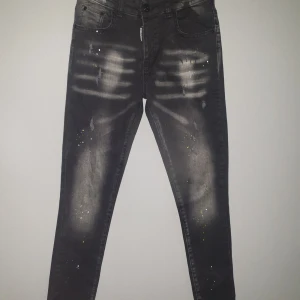 Svarta jeans från Dsquared2 - Snygga svarta jeans från Dsquared2 i nytt skick. De har en cool distressed look med blekta detaljer och färgstänk. Perfekta för en trendig och avslappnad stil. Passar bra till både vardag och fest!