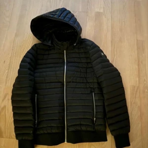 Svart pufferjacka från Moose Knuckles - Säljer en svart pufferjacka från Moose Knuckles i mycket bra skick. Kvitto finns. Jackan har en dragkedja framtill och en mysig huva. Perfekt för kyliga höst- och vinterdagar. Den är quiltad och har långa ärmar för extra värme. Passar både till vardags och lite mer uppklädda tillfällen. Kan gå ner i pris vid snabb affär. Tveka inte på att höra av er vid frågor eller funderingar 