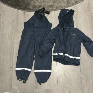 Mörkblå regnställ från True North - Säljer ett mörkblått regnställ från True North, perfekt för blöta dagar. Jackan har huva och dragkedja med knappar, medan byxorna har justerbara hängslen. Båda delarna har reflexdetaljer för extra säkerhet. Använd några gånger men i bra skick!