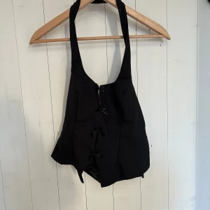 Svart korsettopp - Snygg svart korsettopp med knytning fram. Perfekt för festliga tillfällen! Den har en stilren design med smala axelband och en åtsittande passform. Toppen är i mycket bra skick och redo att bäras till nästa utekväll. Aldrig använd 