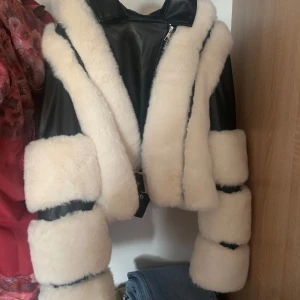 Svart skinnjacka med vit päls från NLY Trend - Säljer en supercool svart skinnjacka med vit fuskpäls från NLY Trend. Jackan har en snygg dragkedja och bälte i midjan. Perfekt för höst och vinter när du vill vara både varm och stilren. Passar perfekt till både fest och vardag! 🖤🤍