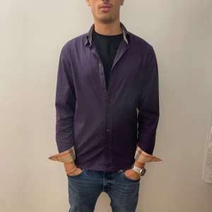 Burberry skjorta - Snygg exklusive lila skjorta med långa ärmar och stilrena knappar. Den har coola rutiga detaljer på insidan av kragen och ärmsluten. Perfekt för både vardag och fest! Passar bra till jeans för en avslappnad look.