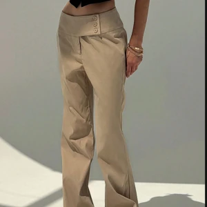Beige kostymbyxor med knappar - Snygga beige kostymbyxor med låg midja. Perfekta för både skola och en kväll ute. Byxorna har en elegant och stilren design med en loose passform som ger en bekväm känsla. Byxorna är endast provade och säljer för de va för små. Skriv privat för egna bilder💕