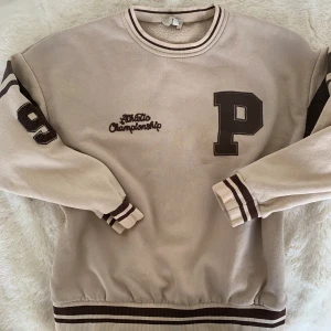 Oversized Beige sweatshirt med bruna detaljer. Beige tröja.  - Oanvänd sweatshirt från pull and bear! Mjukt och mysigt material perfekt nu till hösten eller vintern! Tröjan är oversized 