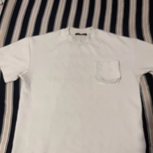 Vit t-shirt från Louis Vuitton - Säljer en stilren vit t-shirt från Louis Vuitton. Den har en liten bröstficka och är i ett mjukt material. Skriv dm om pris