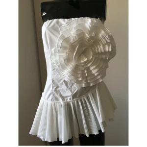 Vit axelbandslös topp/korsett från Mochy - Säljer en superfin vit korsett/topp ifrån Mochy i storlek S/M. Toppen har en unik design med en stor volangdetalj i form av en blomma framtill och plisserad nederdel. Perfekt för en elegant kväll ute. Helt ny med taggar kvar! Säljer då den är för stor för mig som vanligtvis har XS och S! Passar mer S/M!❤️ köpt för ca 1450