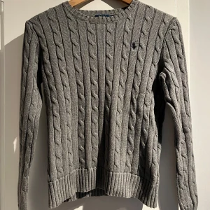 Grå kabelstickad tröja från Ralph Lauren - Grå kabelstickad tröja från Ralph Lauren med mörkblått märke. Fint skick. Storlek XS