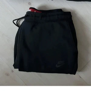 Svart hoodie och byxor från Nike - Säljer ett set med svart hoodie och matchande byxor från Nike. Hoodien har dragkedja och en klassisk design med huva. Perfekt för en avslappnad stil eller träning. Byxorna har en bekväm passform med resår i midjan. Båda plaggen är i mycket bra skick.