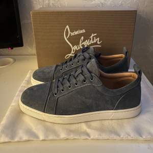 Säljer ett par snygga blå sneakers från Christian Louboutin i mocka. De har en klassisk design med snörning och en röd sula som ger en stilren look. Perfekta för både vardag och festliga tillfällen. Skorna är i mycket bra skick och kommer med originalkartong.