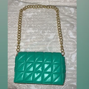 Turkos quiltad axelväska med guldkedja - Snygg turkos axelväska i quiltat mönster med en lyxig guldkedja som axelrem. Väskan har en praktisk dragkedja inuti för säker förvaring. Perfekt för att ge en färgklick till din outfit! Går att pruta.
