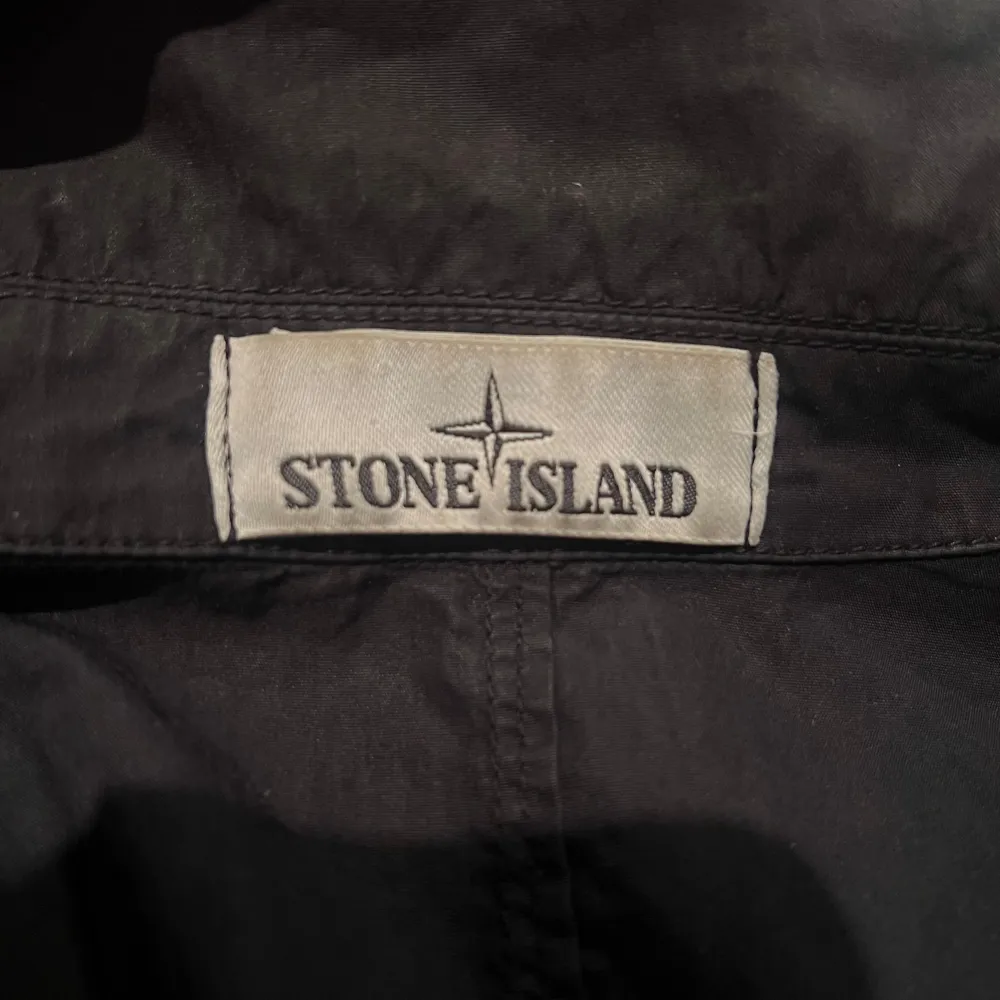 Säljer svart jacka från Stone Island i bra skick. Den har en klassisk krage och en praktisk bröstficka. Perfekt för höst, vår, sommar och vinter med en broderad logga på ärmen. . Jackor.