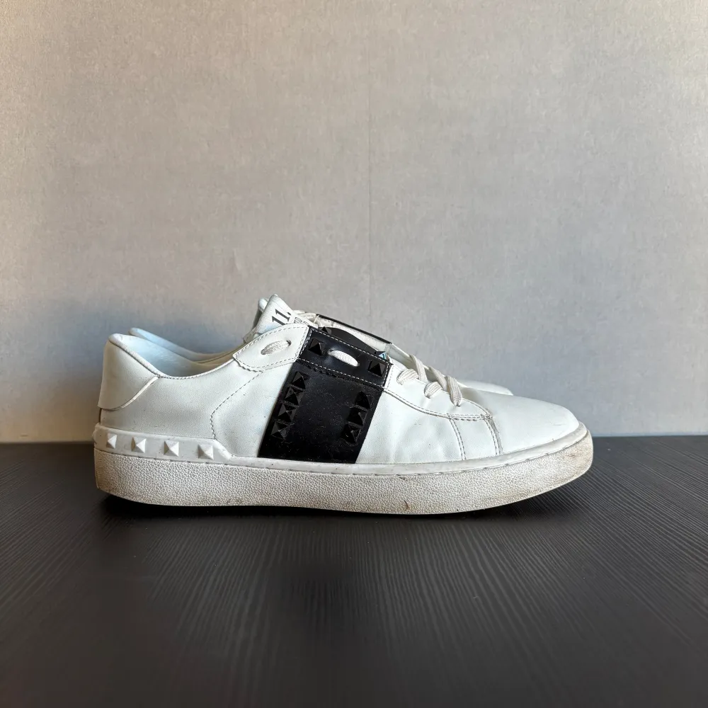 Säljer ett par snygga vita Valentino Rockstud Untitled sneakers i skinn. De har coola svarta detaljer och de ikoniska nitarna på sidan. Skorna är i bra skick med lite slitage på sulan. Perfekta för både vardag och fest!. Skor.