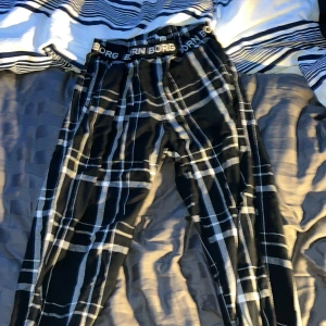 Svarta rutiga pyjamasbyxor från Björn Borg - Säljer ett par svarta rutiga byxor från Björn Borg i storlek 146/152. Byxorna har ett elastiskt midjeband med Björn Borg-loggan och är perfekta för en avslappnad stil. De är i mycket bra skick och passar bra för både vardag och mysiga hemmakvällar. 