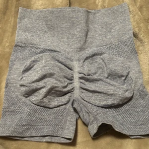 Grå träningsshorts med scrunch - Säljer ett par grå träningsshorts i mycket bra skick. De är högmidjade och har en scrunch-detalj bak som ger en snygg passform. Perfekta för gymmet eller yoga! Materialet är stretchigt och bekvämt. Passar till S med.