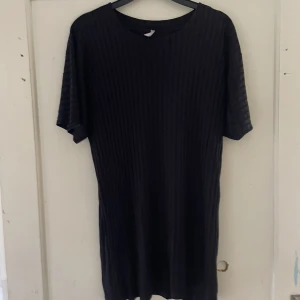 Svart ribbad topp - Säljer en svart ribbad topp med korta ärmar. Den är perfekt för både vardag och festliga tillfällen. Materialet är mjukt och stretchigt, vilket gör den bekväm att bära hela dagen.