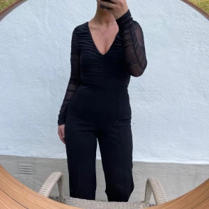 Svart långärmad body - Säljer en elegant svart body med långärmade och en djup v-ringning. Den har en snygg rynkad detalj framtill som ger en smickrande passform. Perfekt för en utekväll eller fest!