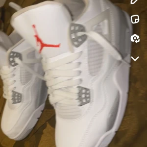 Vita Nike Air Jordans med röd logga - Säljer ett par snygga vita Jordan 4 white oreo.  Skorna är i skinn och har klassisk snörning. Perfekta för både vardag och fest! Jag söker dem för jag söker ett par nya. Jag har använt dem 2 gånger under sommaren så skick 9,9 