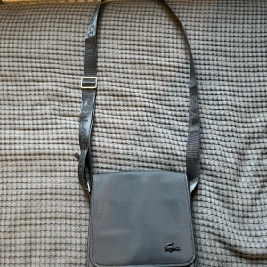 Svart axelväska från Lacoste - Säljer en stilren svart axelväska från Lacoste. Den är helt ny, köpte för 1600 säljer för 900. Helt ny och oanvänd 
