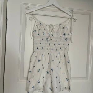 Somrig jumpsuit storlek 36 - En jättegullig vit jumpsuit med små blåa blommor från hm. Axelbanden går att justera men knutar. Bra skick🌸🌸