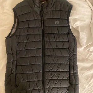 Svart quiltad dunväst från Hangten - Säljer en snygg och praktisk svart quiltad dunväst från Hangten. Perfekt för kyliga dagar med dragkedja framtill. Västen är i storlek S och passar både för höst och vår. Den är i bra skick och redo för nya äventyr!