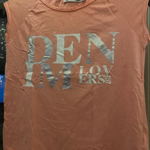 Persikofärgad ärmlös topp med tryck - Säljer en cool persikofärgad ärmlös topp från 157 med texten 'DENIM LOVERS' i metallictryck på framsidan. Perfekt för en avslappnad sommarlook!
