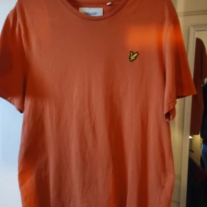 Orange t-shirt från Lyle & Scott - Säljer en snygg orange t-shirt från Lyle & Scott. Den är i bomull och har en liten broderad logga på bröstet. Perfekt för en avslappnad stil!