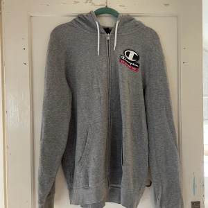 Grå hoodie från Champion - Säljer en grå hoodie från Champion i storlek XL. Den har en dragkedja framtill och en klassisk Champion-logga på bröstet. Perfekt för en avslappnad stil och passar bra till både höst och vår. Den är i bra skick och superbekväm!