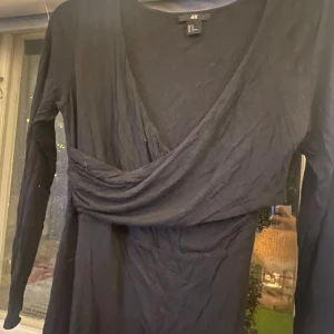 Svart omlottklänning från H&M - Säljer en elegant svart omlottklänning från H&M. Klänningen har en v-ringad design och långa ärmar, perfekt för både vardag och fest. Materialet är mjukt och bekvämt, vilket gör den idealisk för höst och vinter. Passar bra till både stövlar och klackar!