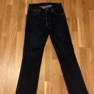 Mörkblå jeans från Nudie Jeans - Säljer ett par snygga mörkblå jeans från Nudie Jeans. De har en klassisk straight fit och är tillverkade i högkvalitativt denim. Jeansen har orange sömmar och en läderpatch med logotypen på baksidan. Perfekta för både vardag och fest!❤️pris diskuteras