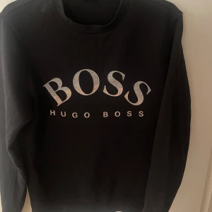 Svart tröja från Hugo Boss - Snygg svart tröja från Hugo Boss med stort BOSS-tryck i silver storlek xs men passar absolut s har ni några frågor kontakta mig gärna priset är ej hugget i sten