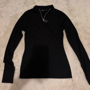 Svart långärmad tröja från Boohoo - Snygg svart långärmad tröja från Boohoo med dragkedja och rund ringdetalj vid halsen. Perfekt för en stilren look. Aldrig använd.