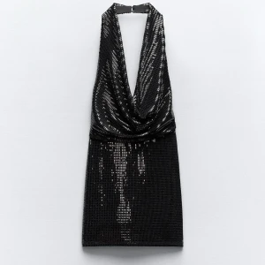Svart paljett klänning - Snygg svart klänning med glittriga paljetter och djup v-ringning. Perfekt för en festlig kväll. Klänningen har en kort längd och är ärmlös med en elegant halterneck-design.