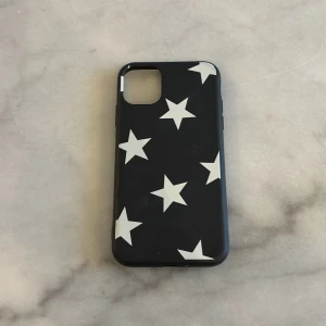 Svart mobilskal med stjärnor till iPhone 11 - Snyggt svart mobilskal dekorerat med vita stjärnor. Perfekt för att ge din telefon en stilren och unik look. Skalet är designat för att skydda din mobil samtidigt som det ger ett trendigt utseende.