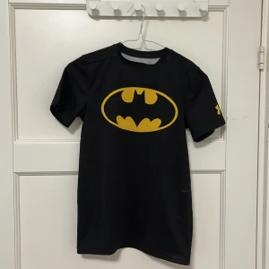 Batman träningströja - Fin tränings-t-shirt från Under Armour med Batman-tryck på framsidan. Bra skick. Sitter figurnära och är storlek 14år. Funkar även XS skulle jag säga
