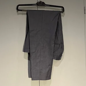 Blå kostymbyxor från Tiger of Sweden - Grå/blå kostymbyxor från Tiger of Sweden med en smal passform. Storlek 38. Förkortad för att passa 156cm.