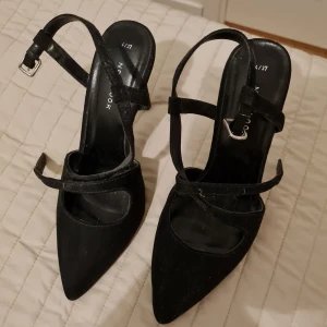 Svarta pumps med remmar - Eleganta svarta pumps från New Look med spetsig tå och smala remmar. Skorna har en hög klack och justerbara spännen för perfekt passform. Perfekta för en stilren look.